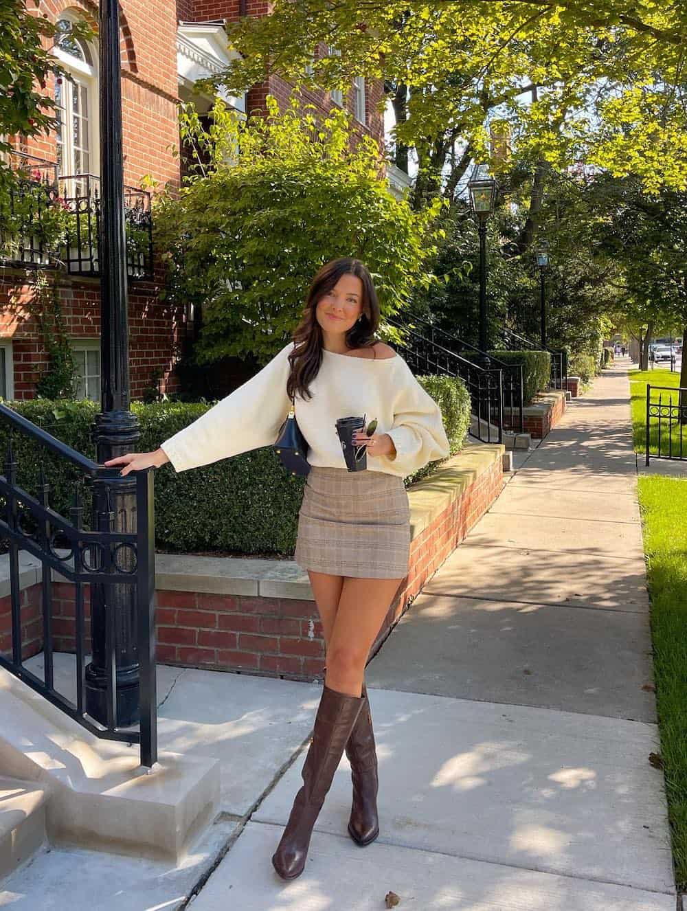 Woman wearing a plaid mini skirt with an off the shoulder sweater and tall brown boots.