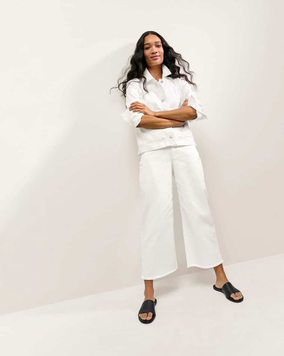 A Black woman wearing a white denim jacket with white jeans and black sandals