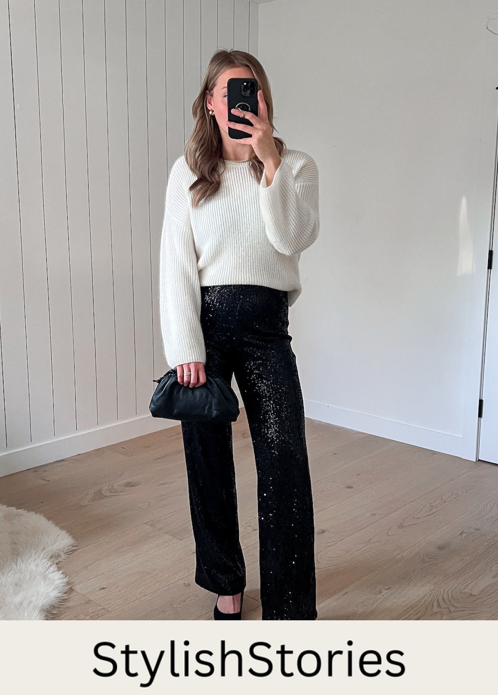 A woman wearing sparkly black wide-leg pants with a white knit crewneck sweater, black heels, and a dark green clutch