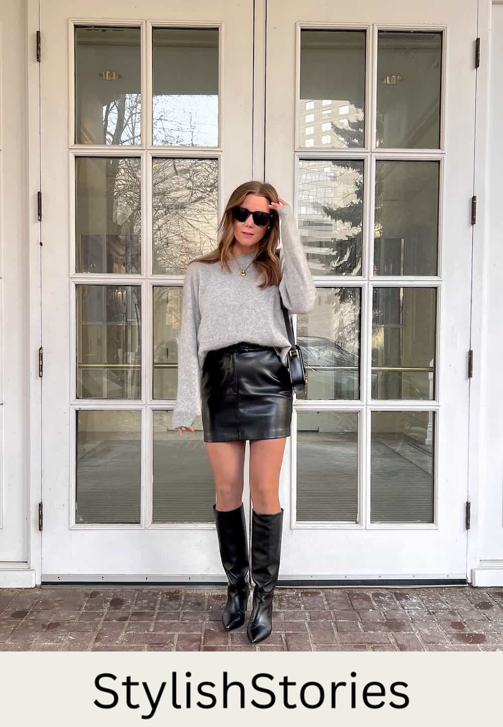 A woman wearing a black leather mini skirt with a light grey crewneck sweater and knee-high black leather boots