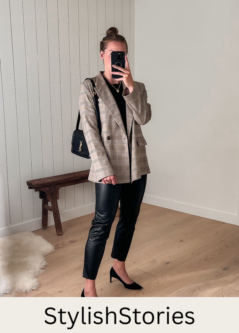 A woman wearing black leather pants, a black crewneck top, and a grey and beige plaid blazer with black heels