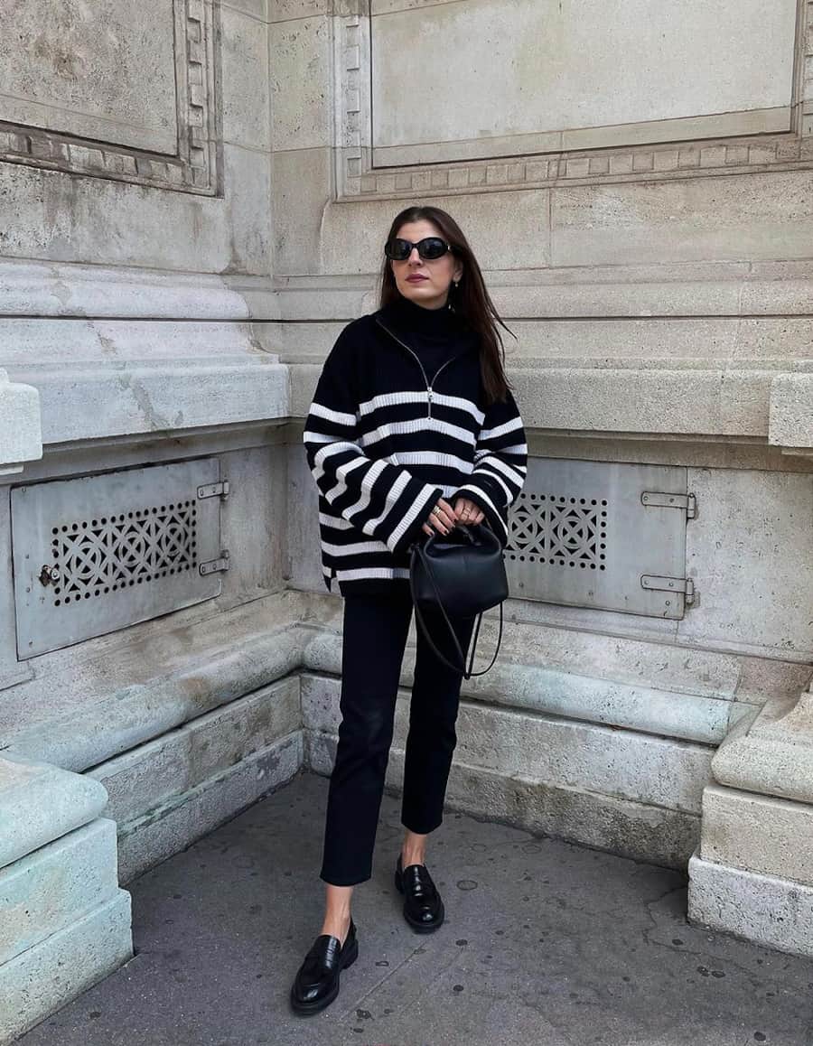 image of a woman in an oversized striped knit sweater, black trousers, and a pair of black loafer shoes