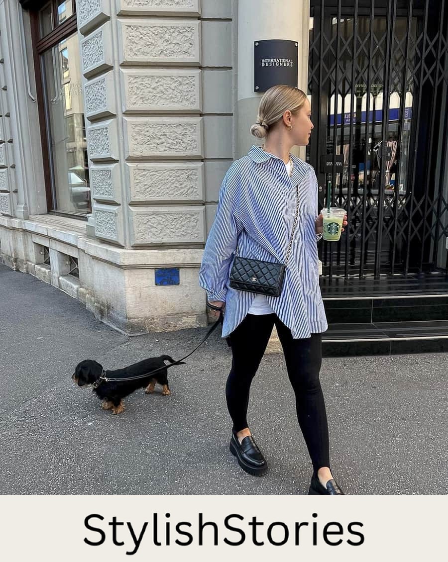 image of a woman walking her dog wearing a striped oversized button up shirt, black leggings with stirrup detail and black chunky style loafers