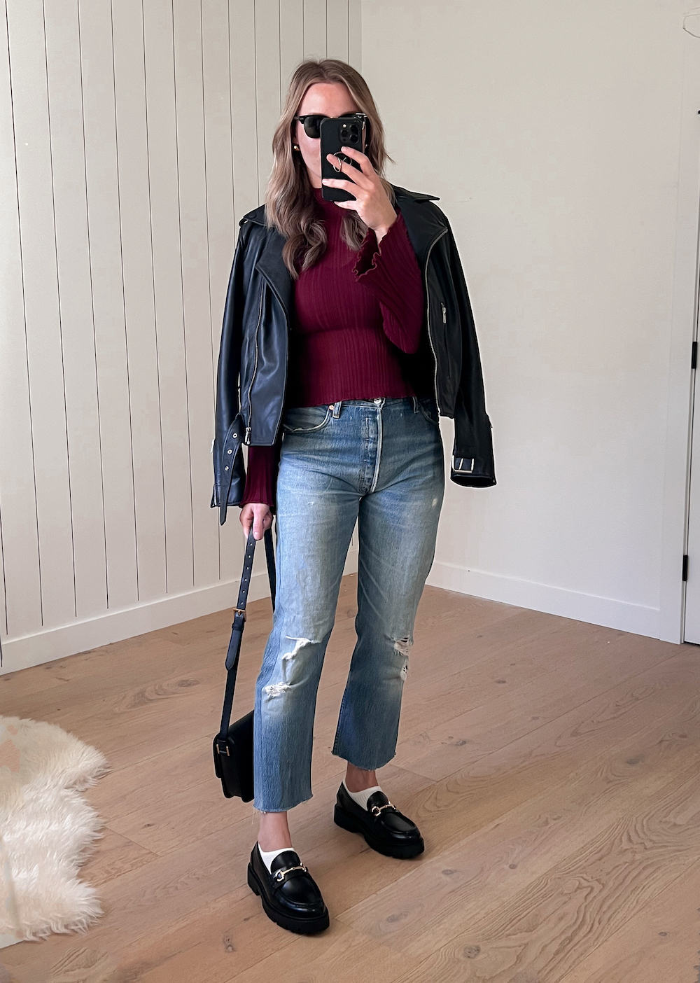 woman wearing distressed jeans and black chunky loafers with a cranberry sweater under a leather jacket.