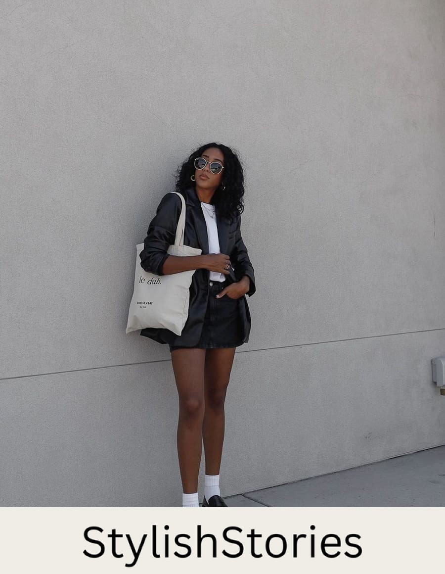 image of a black woman in a black leather blazer, white t-shirt, black denim skirt, white ankle socks, and chunky black flats