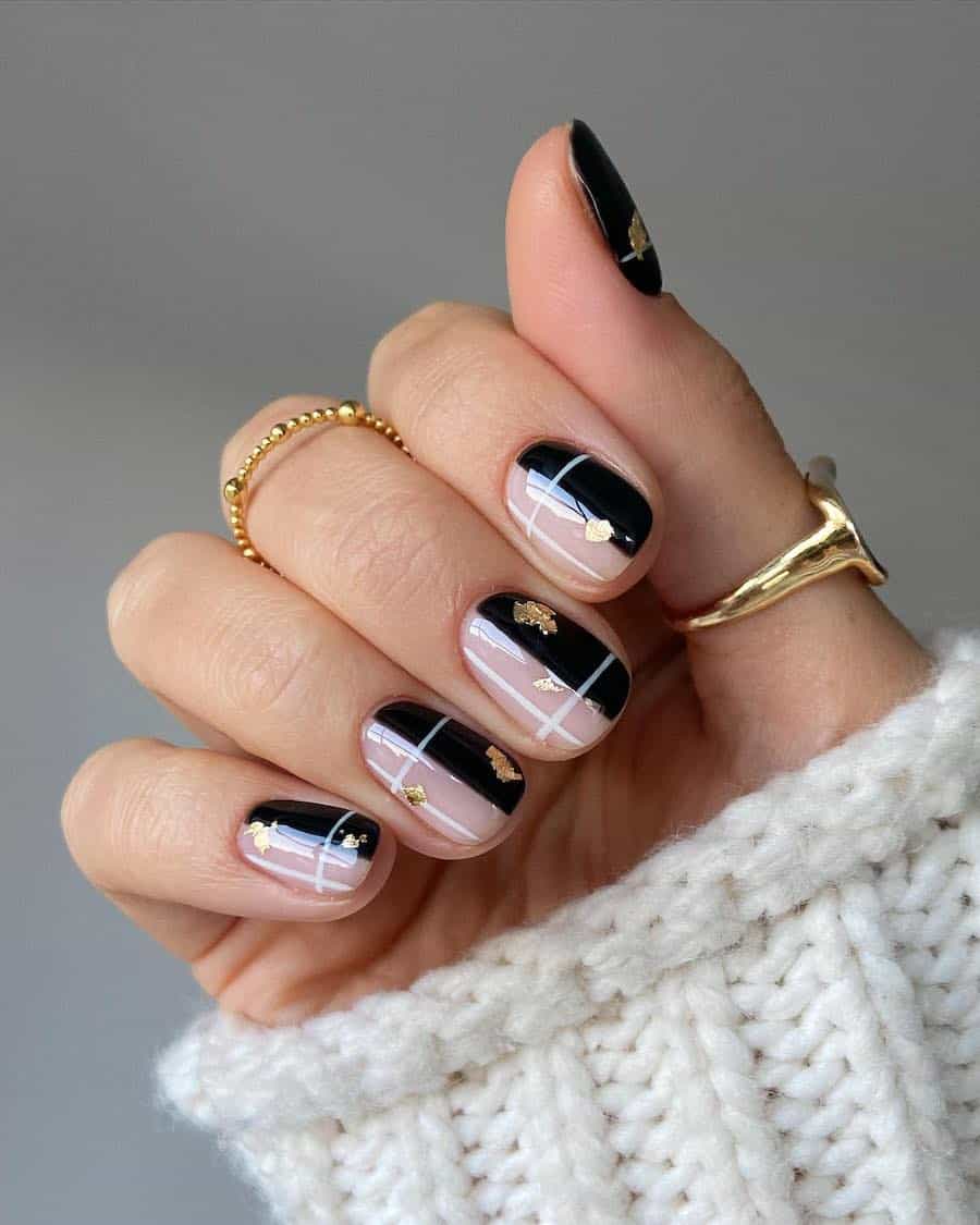 A hand with short round nails painted half nude and half black with white grid details and gold flakes