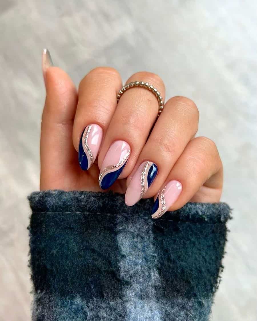 A hand with medium almond nails painted a nude pink with navy and gold glitter waves