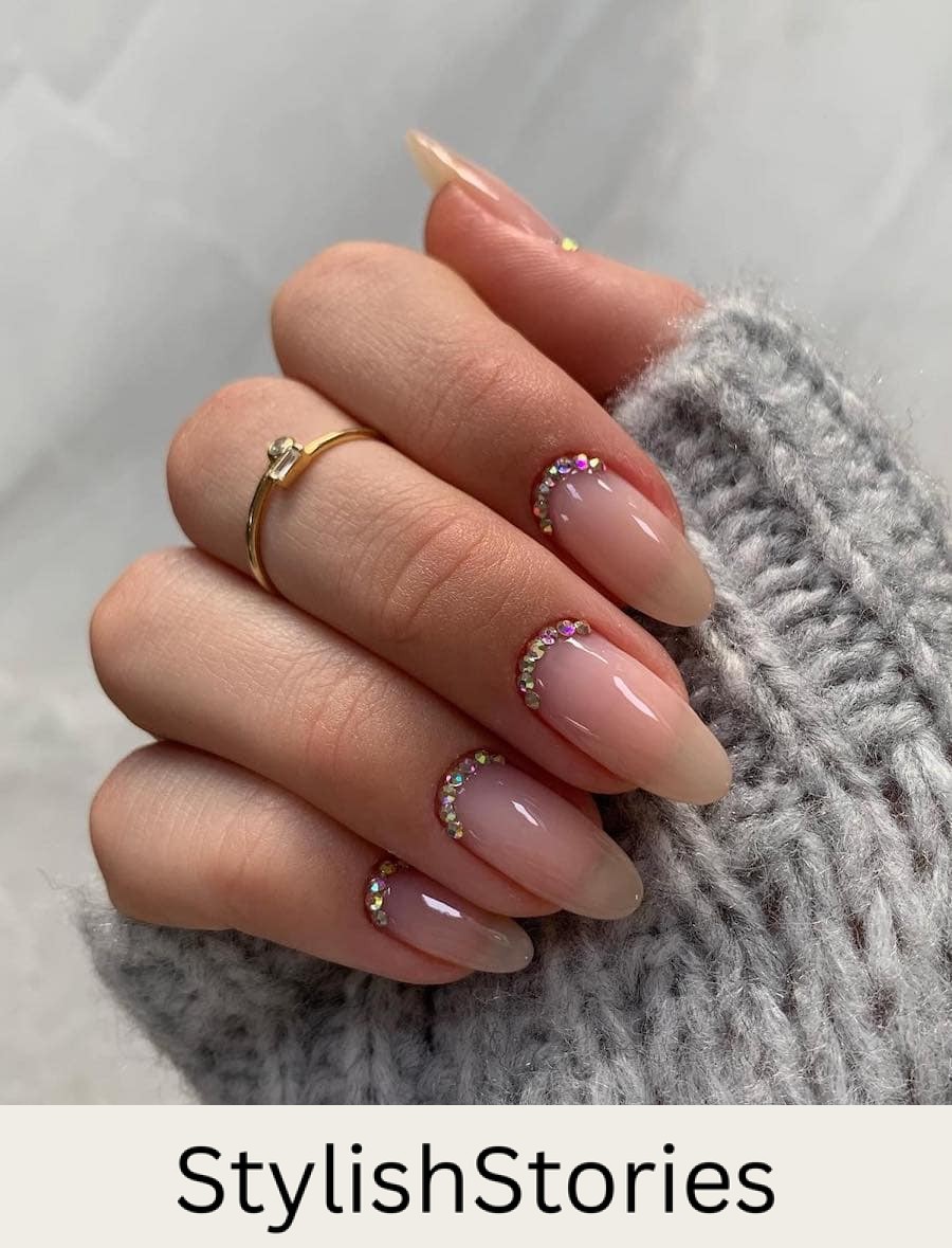 A hand with glossy nude almond nails with crystal reverse French tips