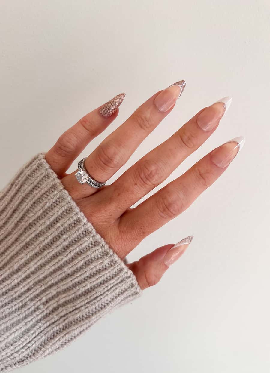 A hand with medium nude almond nails with white and gold glitter French tips and a gold glitter accent nail