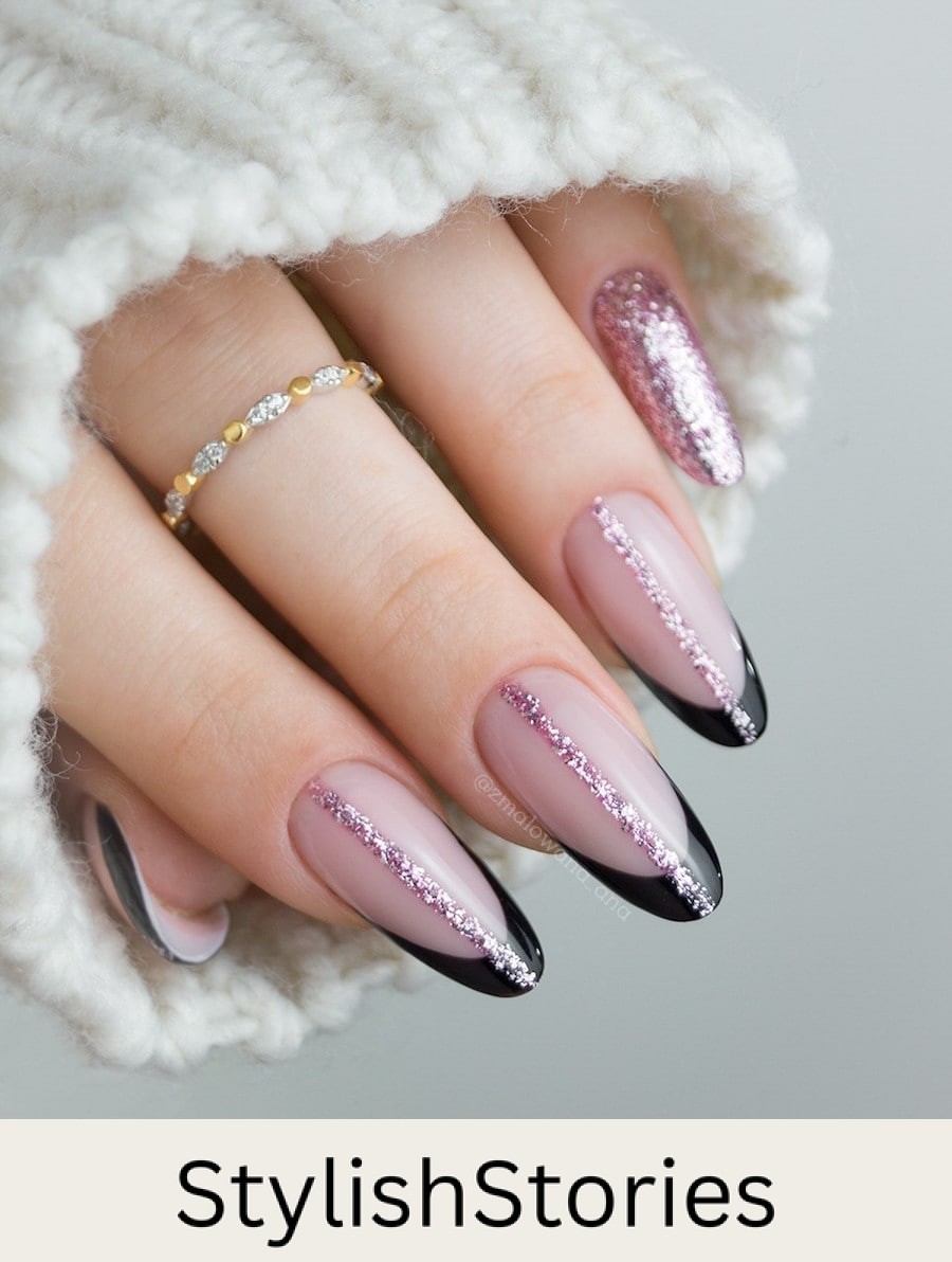 A hand with long nude pink almond nails with black French tips and vertical pink glitter lines down the center of each nail