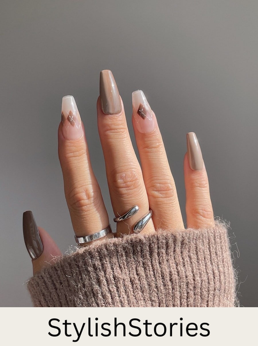 A hand with long coffin nails painted in glossy brown polish with two clear nails with brown and white lined diamond patterns