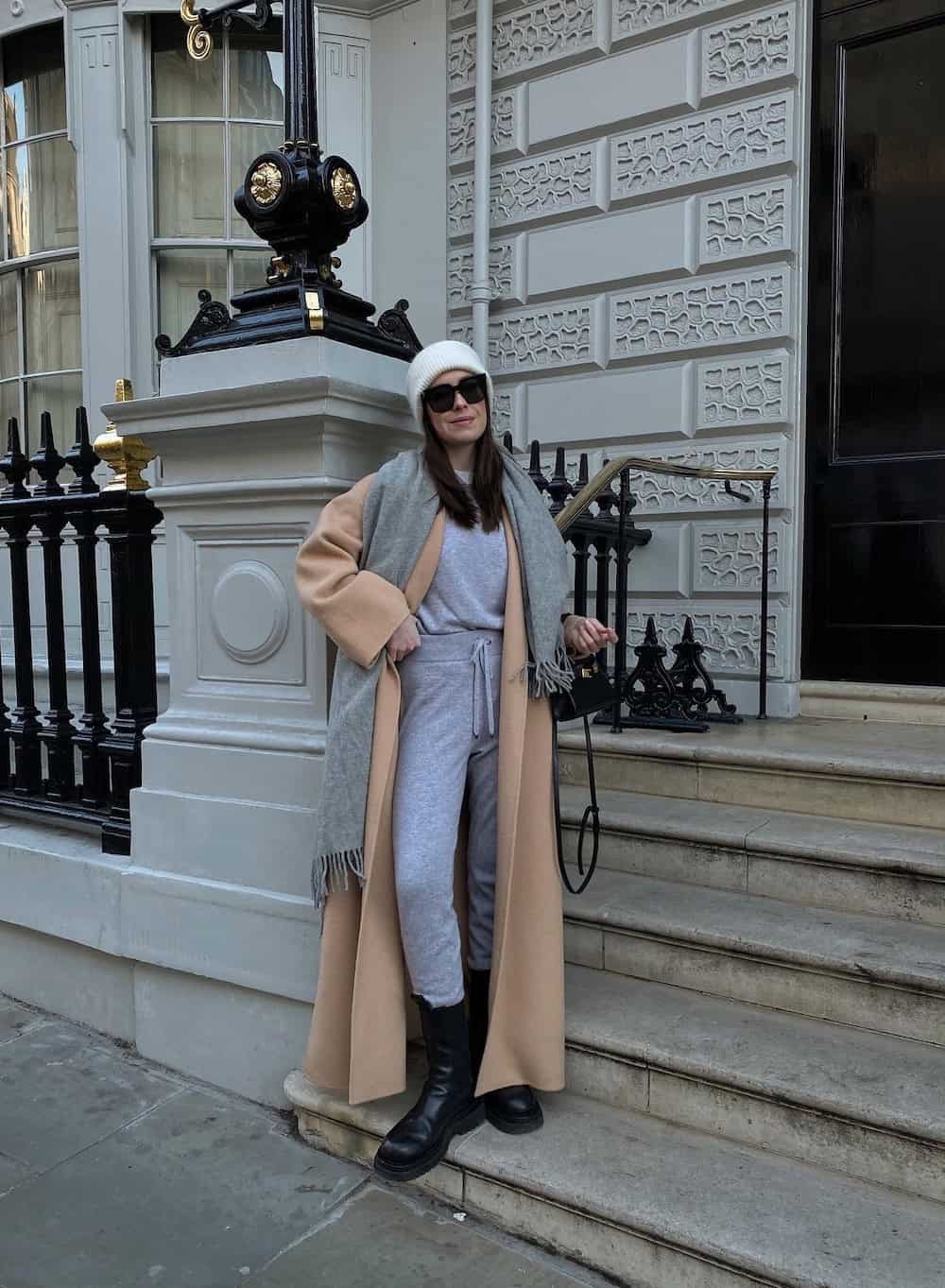 Woman wearing a matching sweat set with a long cardigan jacket, a grey scarf and black boots.