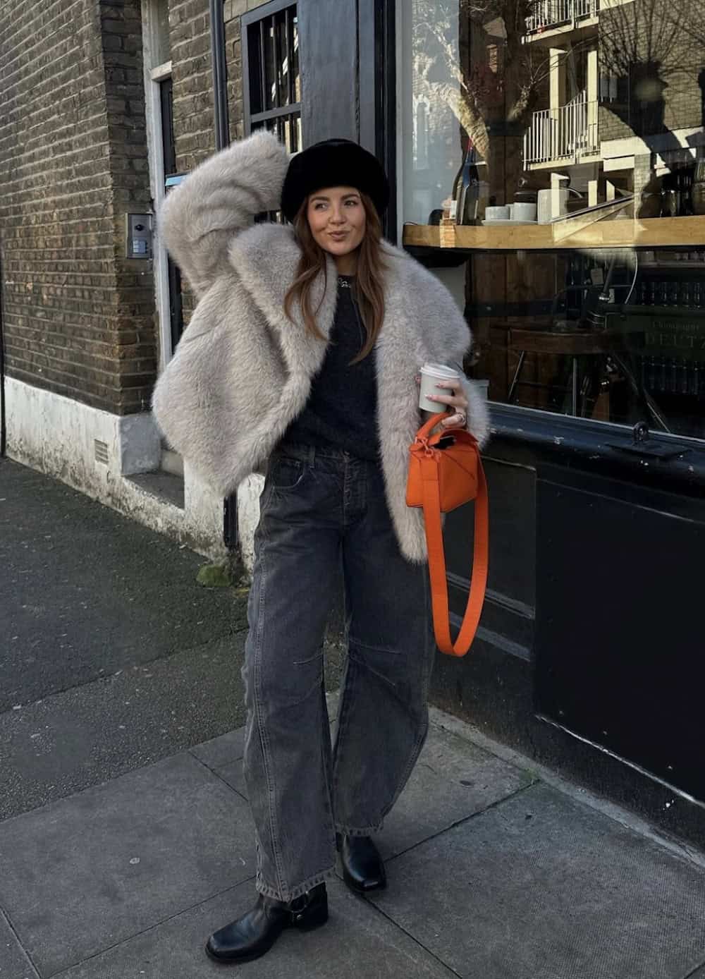 Woman wearing oversized black jeans with a faux fur jacket and black hat.