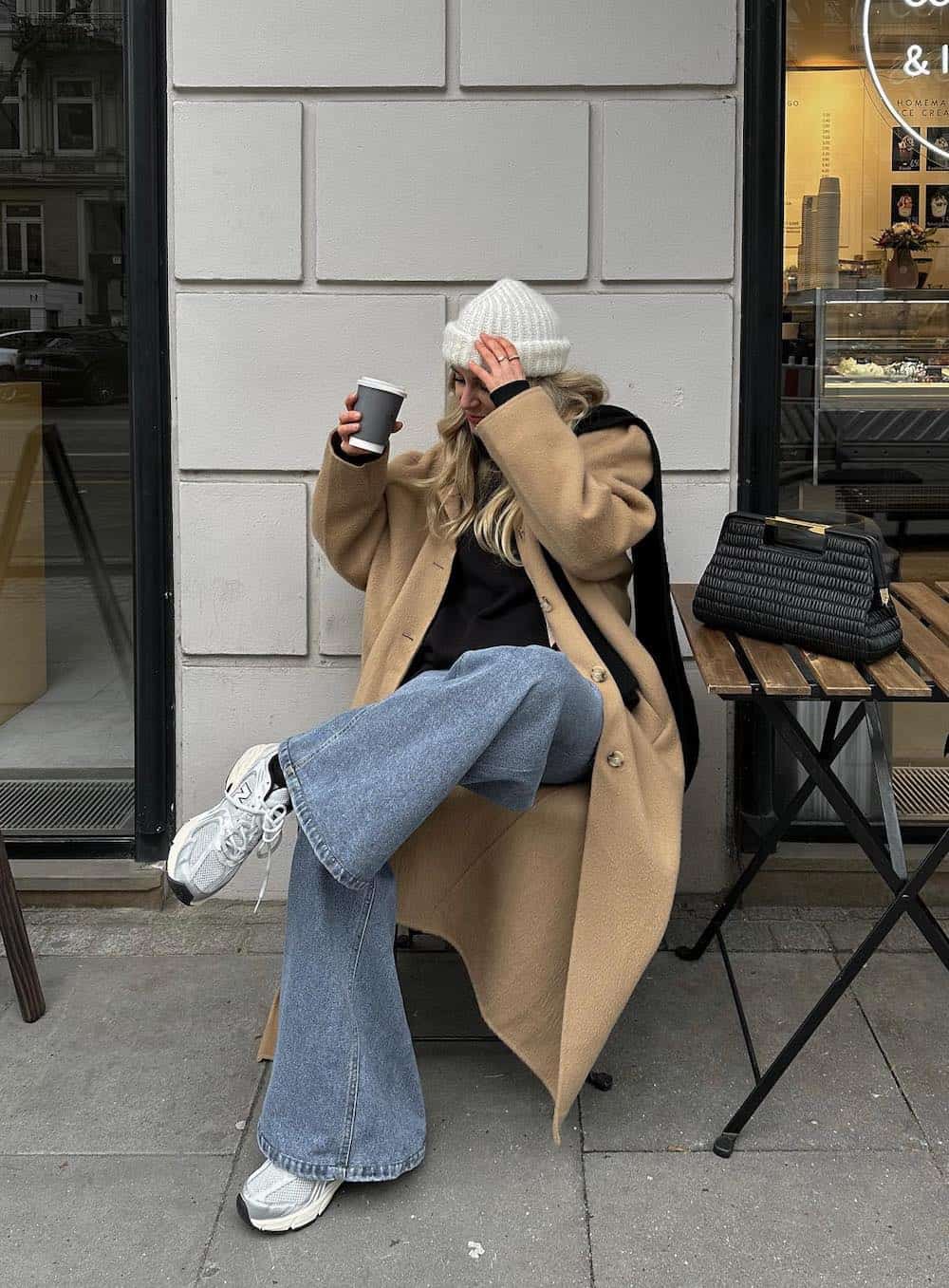 Woman wearing wide leg jeans with a black sweater and an oversized trench coat.