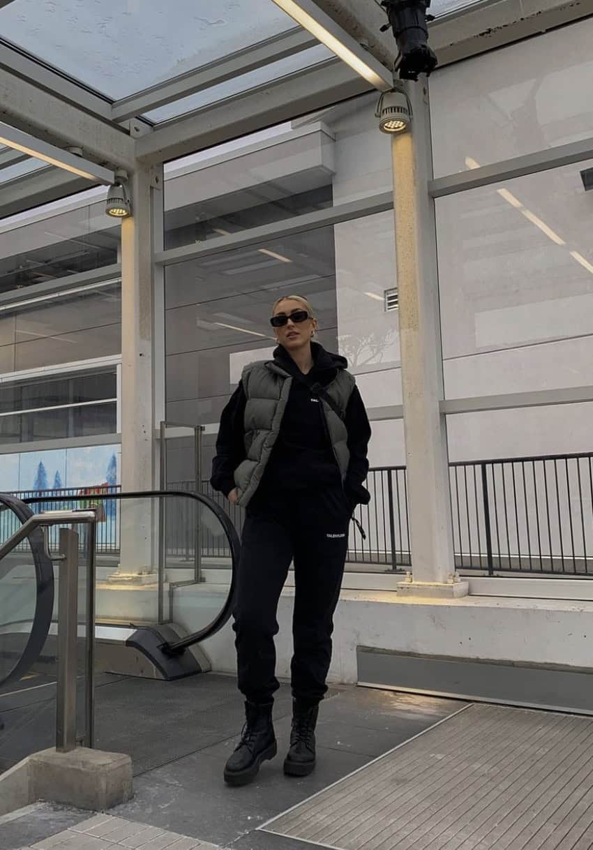 Woman wearing black sweat pants, a black hoodie and a grey puffer vest with moon boots.