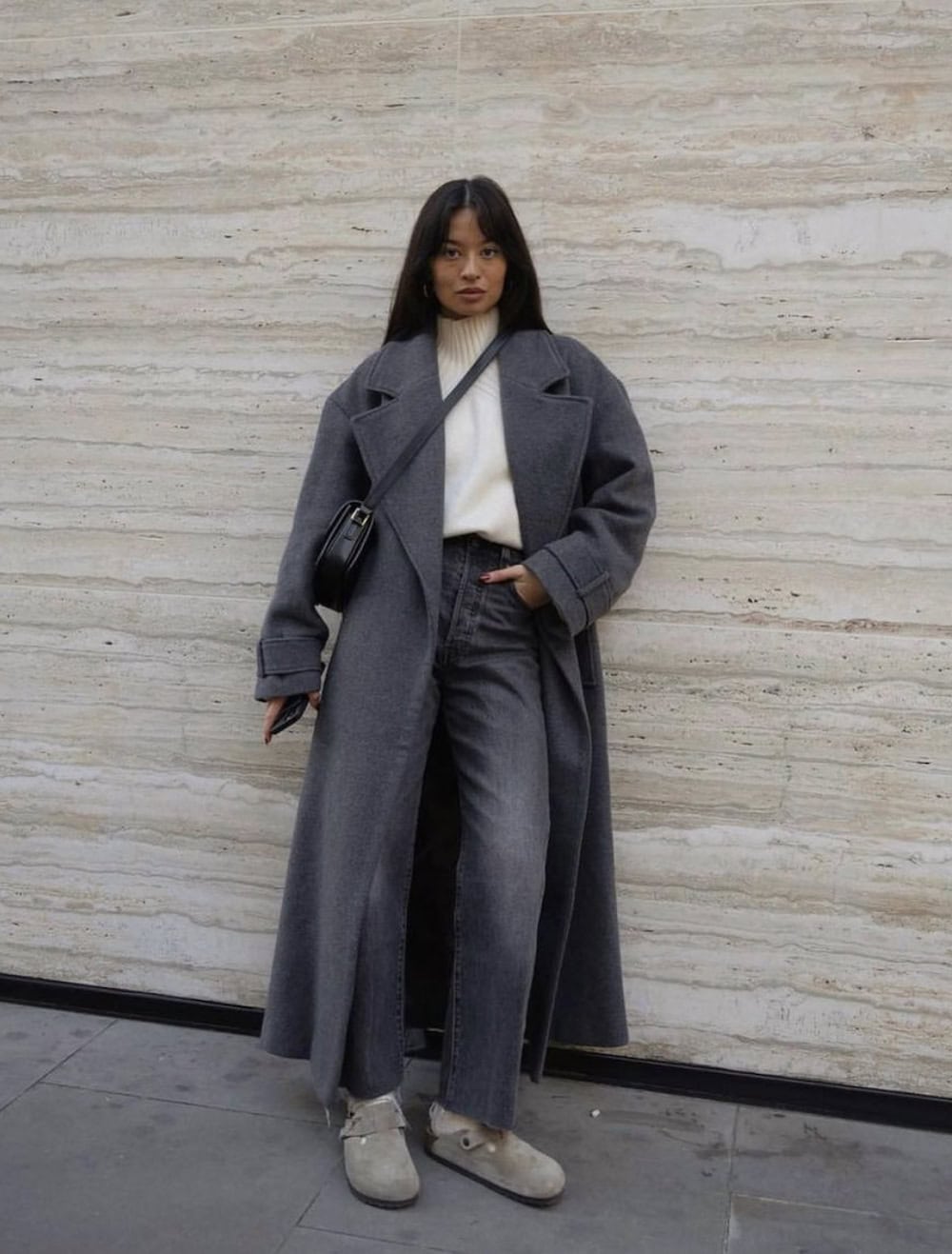 Woman wearing jeans with a turtle neck sweater and a long goat with Birkenstocks.