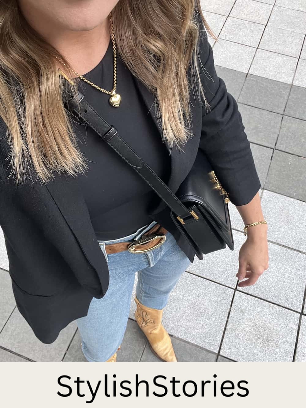 Overhead image of a woman wearing a country concert outfit with a black bodysuit, black blazer, brown suede belt, jeans, and brown cowboy boots