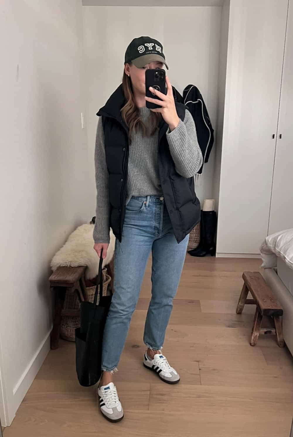 woman wearing jeans, a gray sweater, sneakers and a black puffer vest.