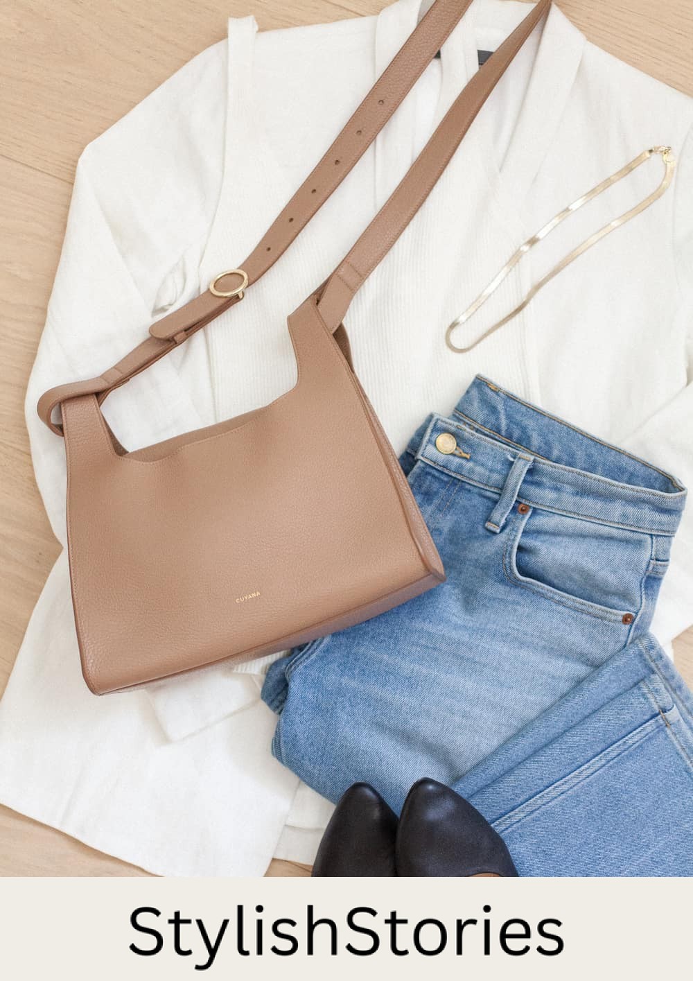 image of an outfit flatlay with a light brown leather Cuyana bag with a white blazer, blue jeans, black flats, and a gold necklace