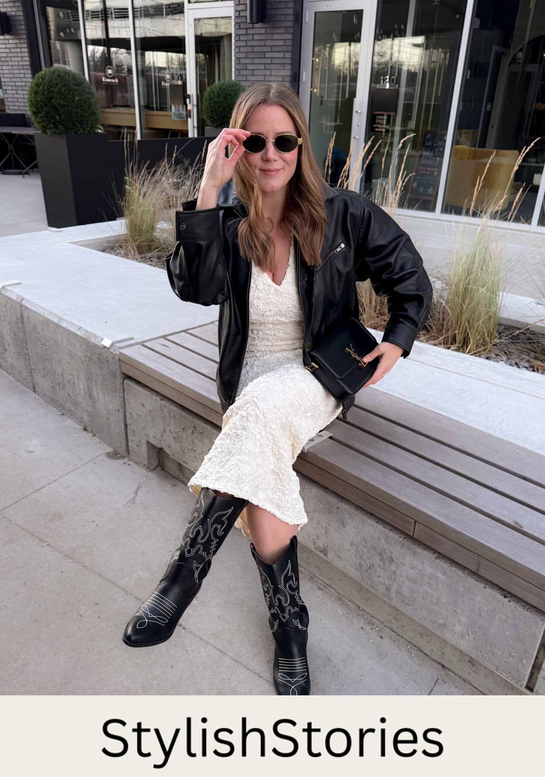 Christal wearing a white midi dress with a black leather jacket and black western boots.