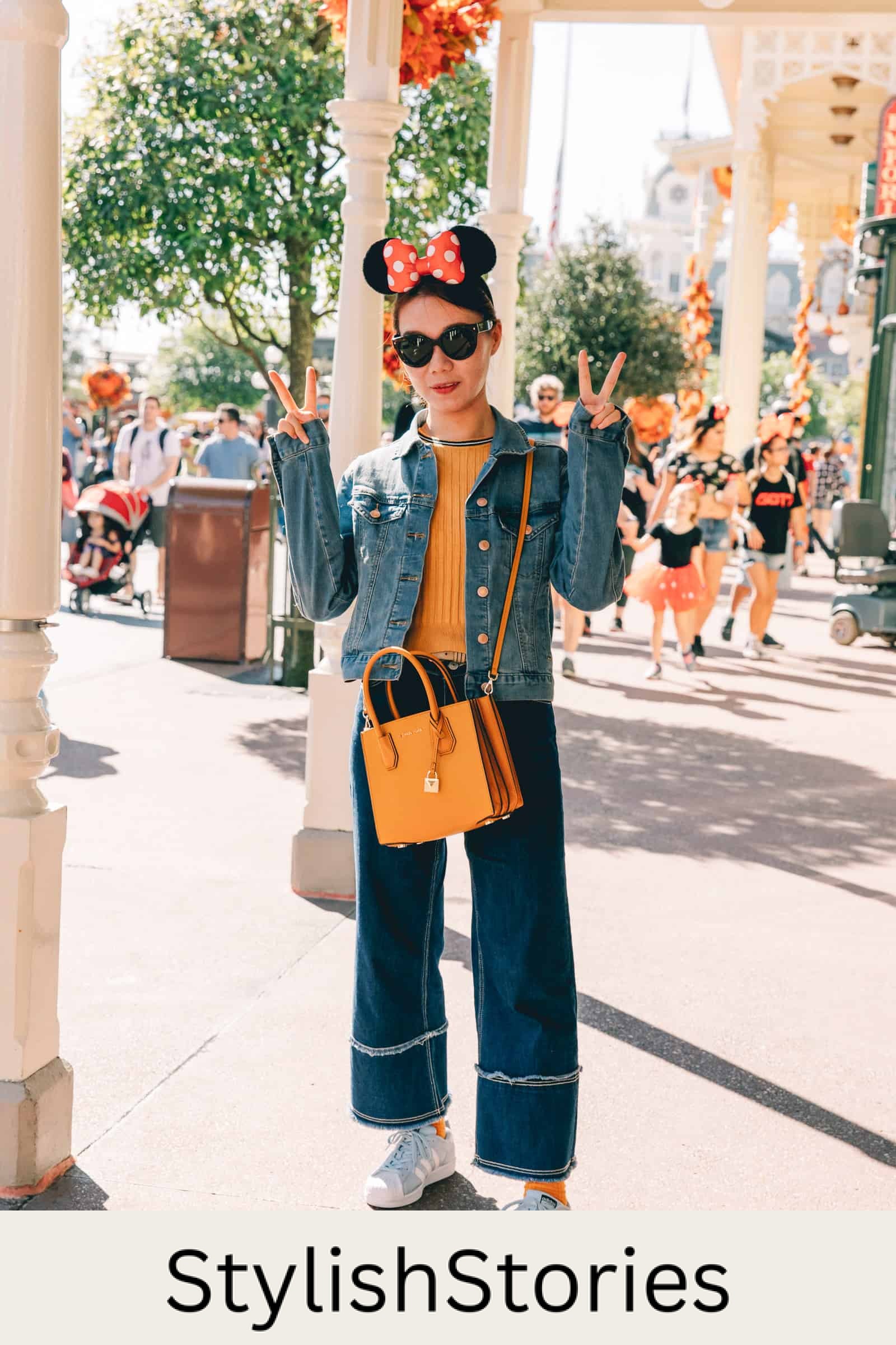 woman wearing a jean jacket, orange sweater, blue jeans, and sneakers with Minnie Mouse ears at Disneyland