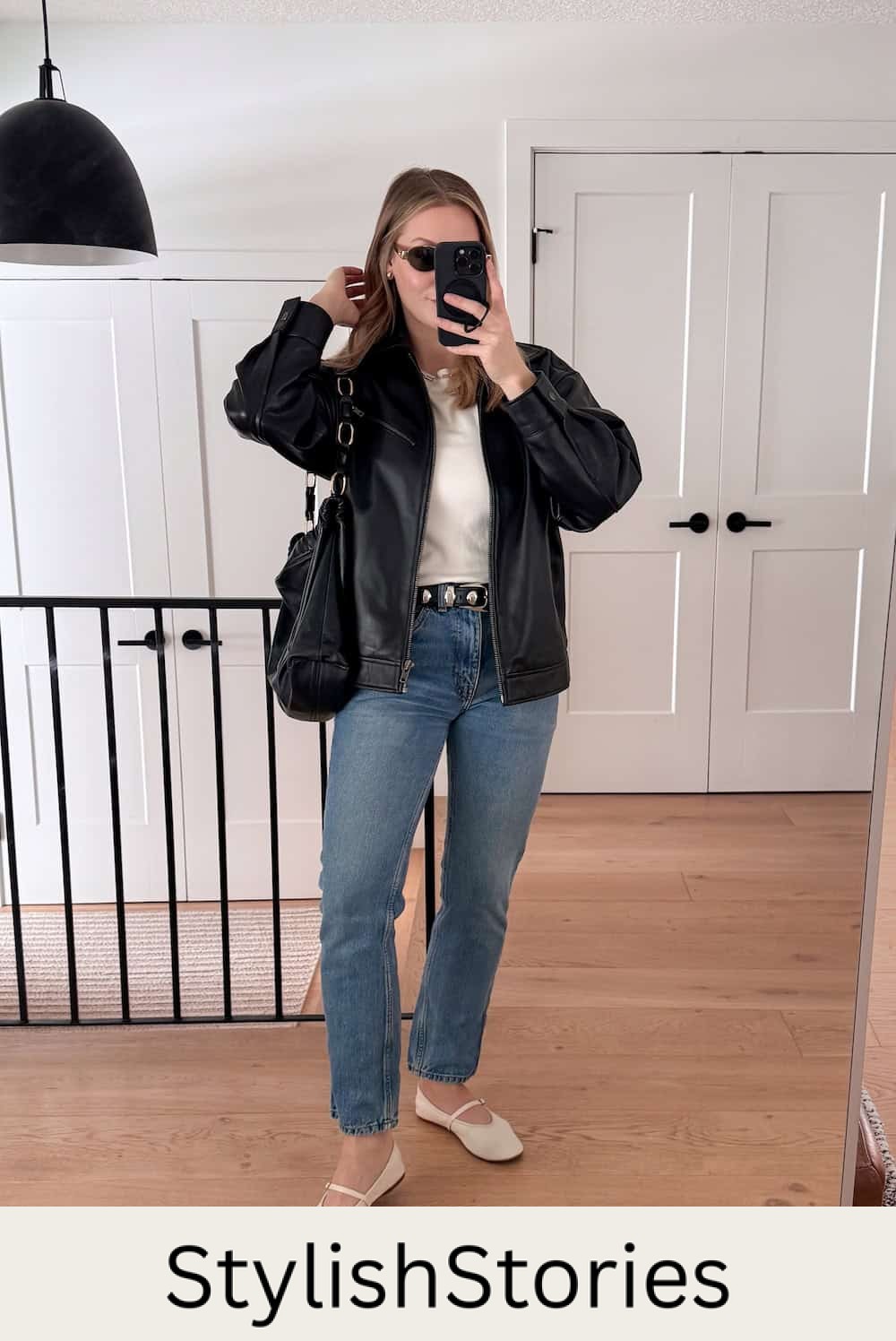 Woman wearing jeans, a white top, a black leather jacket and white flats.
