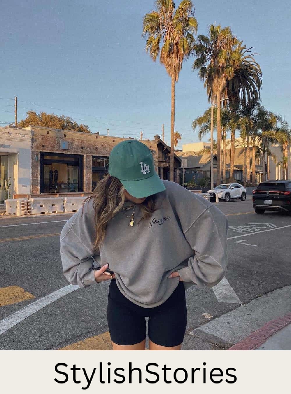 Woman wearing biker sorts, a crew neck sweatshirt and a baseball cap.