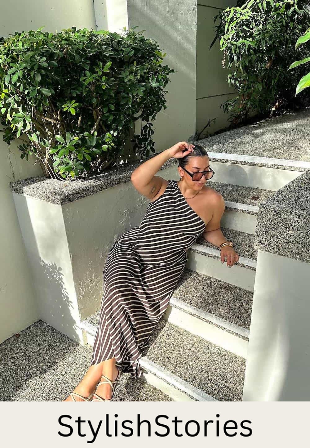 Woman wearing a black and white striped, one shoulder maxi dress with sandals.