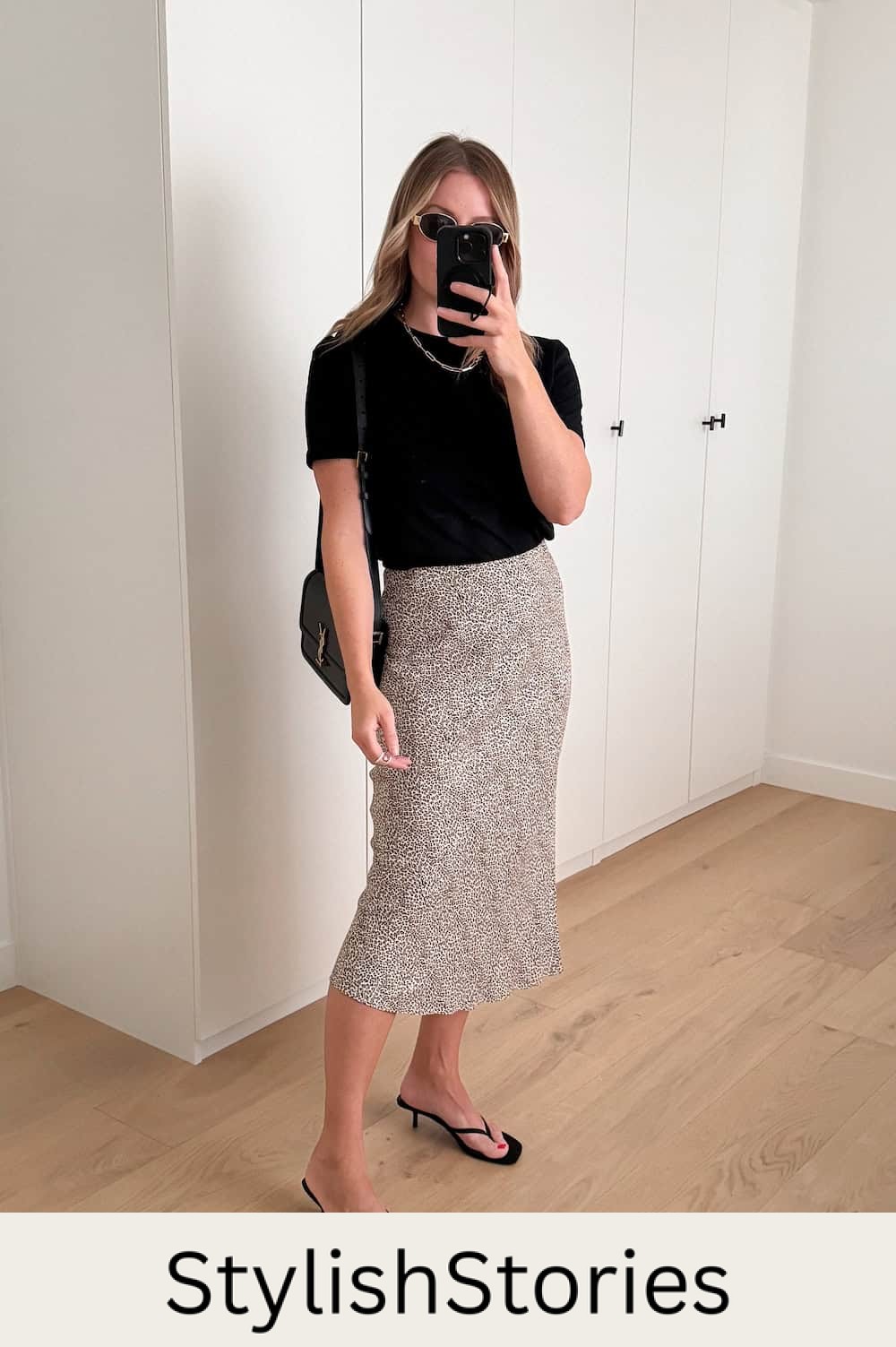 Woman wearing a printed slip skirt with a black t-shirt and black heeled sandals.
