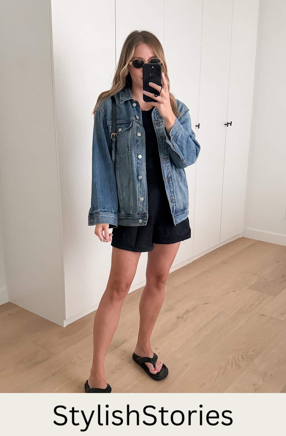 Christal wearing black shorts and a black tank top with a denim jacket and sandals.