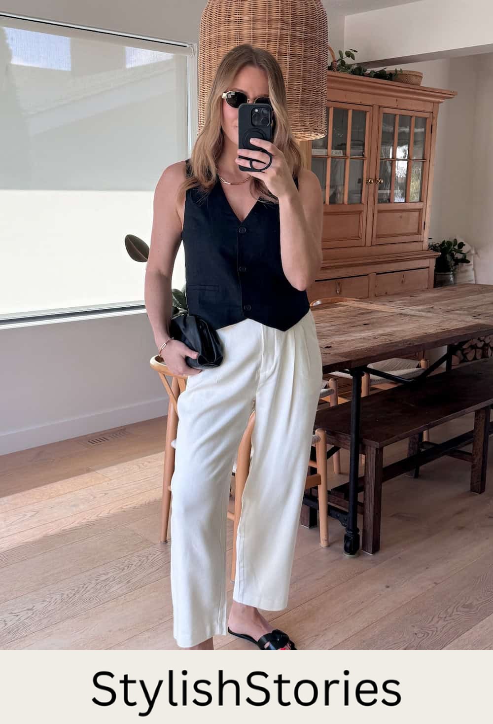 Christal wearing white tailored pants with a black vest top and black sandals.