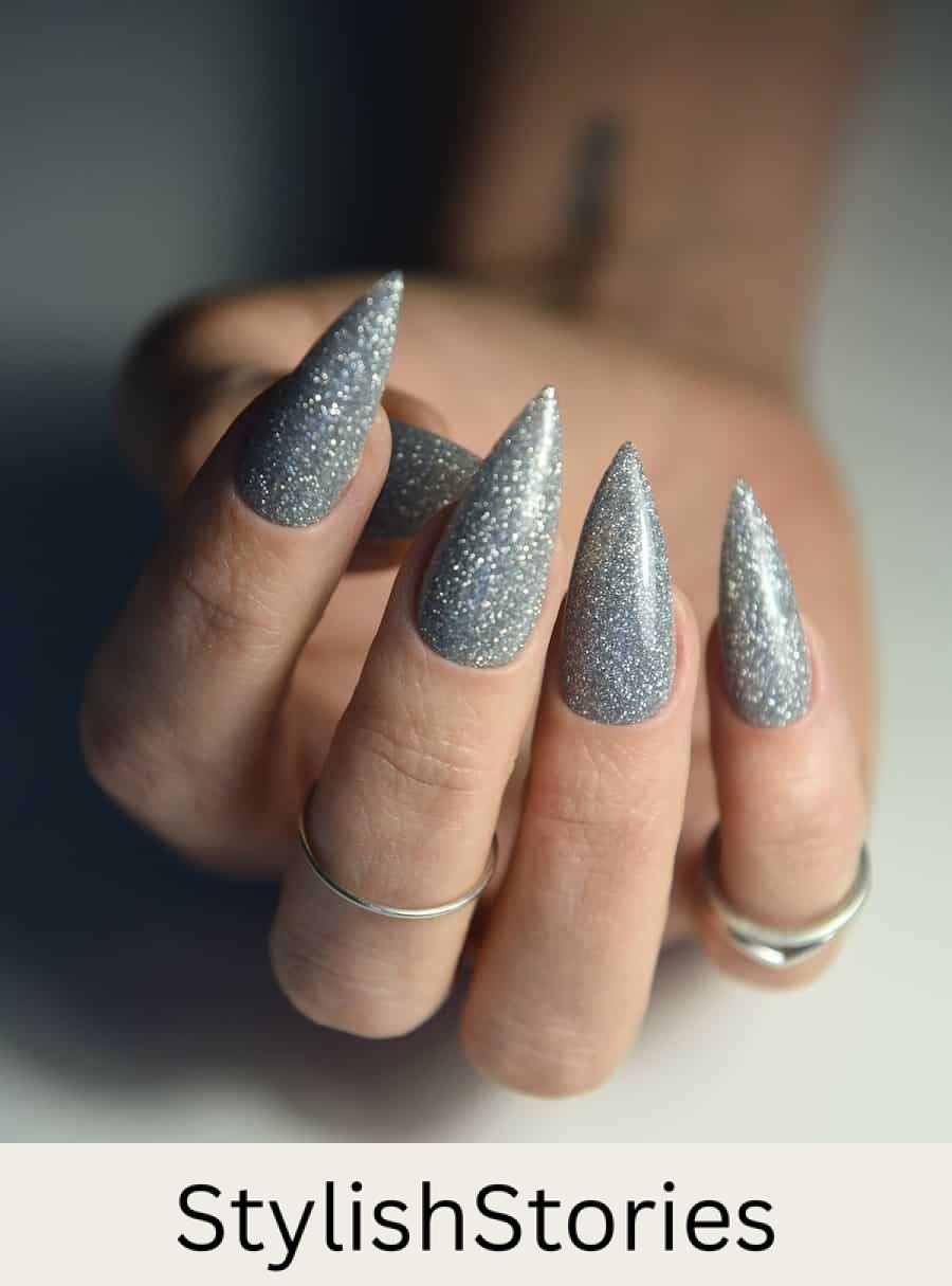 A hand with long stiletto nails painted with silver glitter nail polish