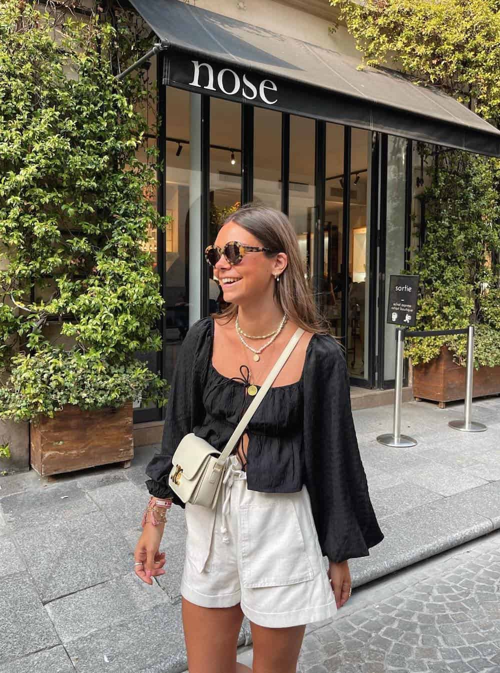Woman wearing white linen shorts, a black cropped blouse and white accessories.