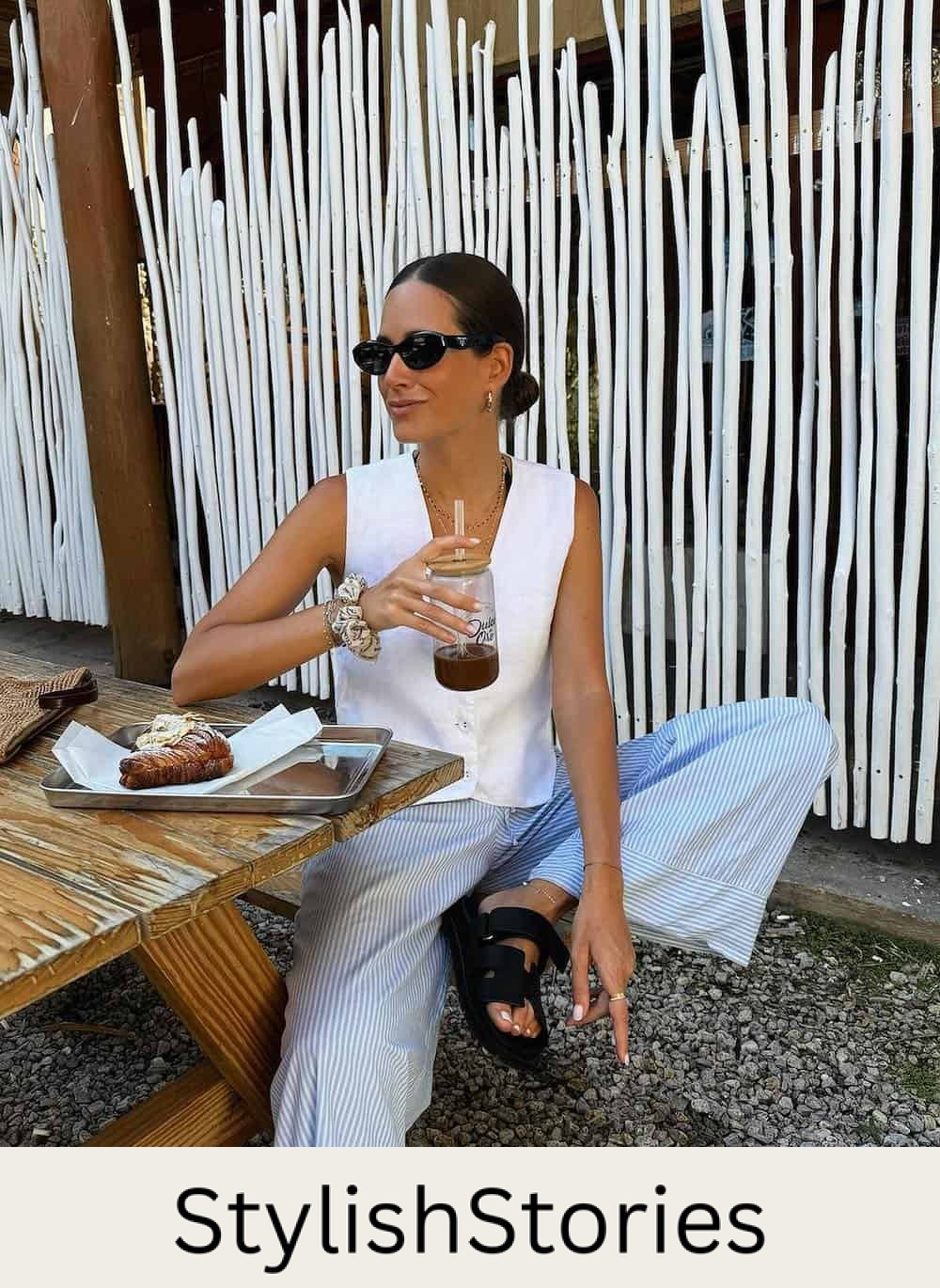 Woman eating lunch at a picnic table wearing blue and whites striped pants and a white vest top.