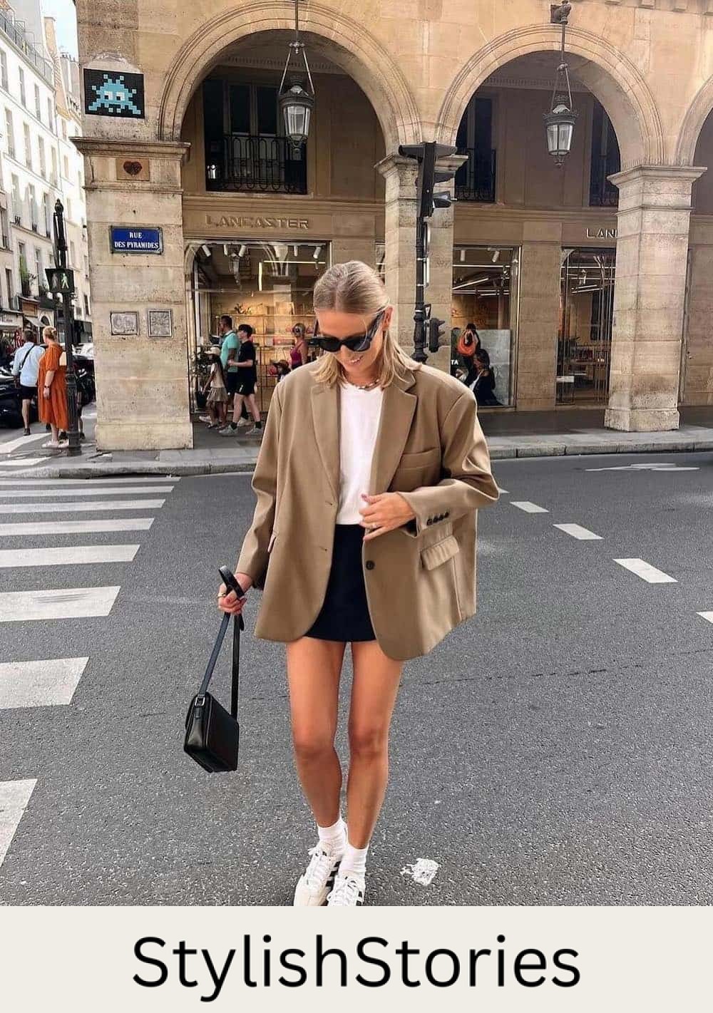 Woman walking in the street wearing a black skirt, a white t-shirt and an oversized blazer with sneakers.