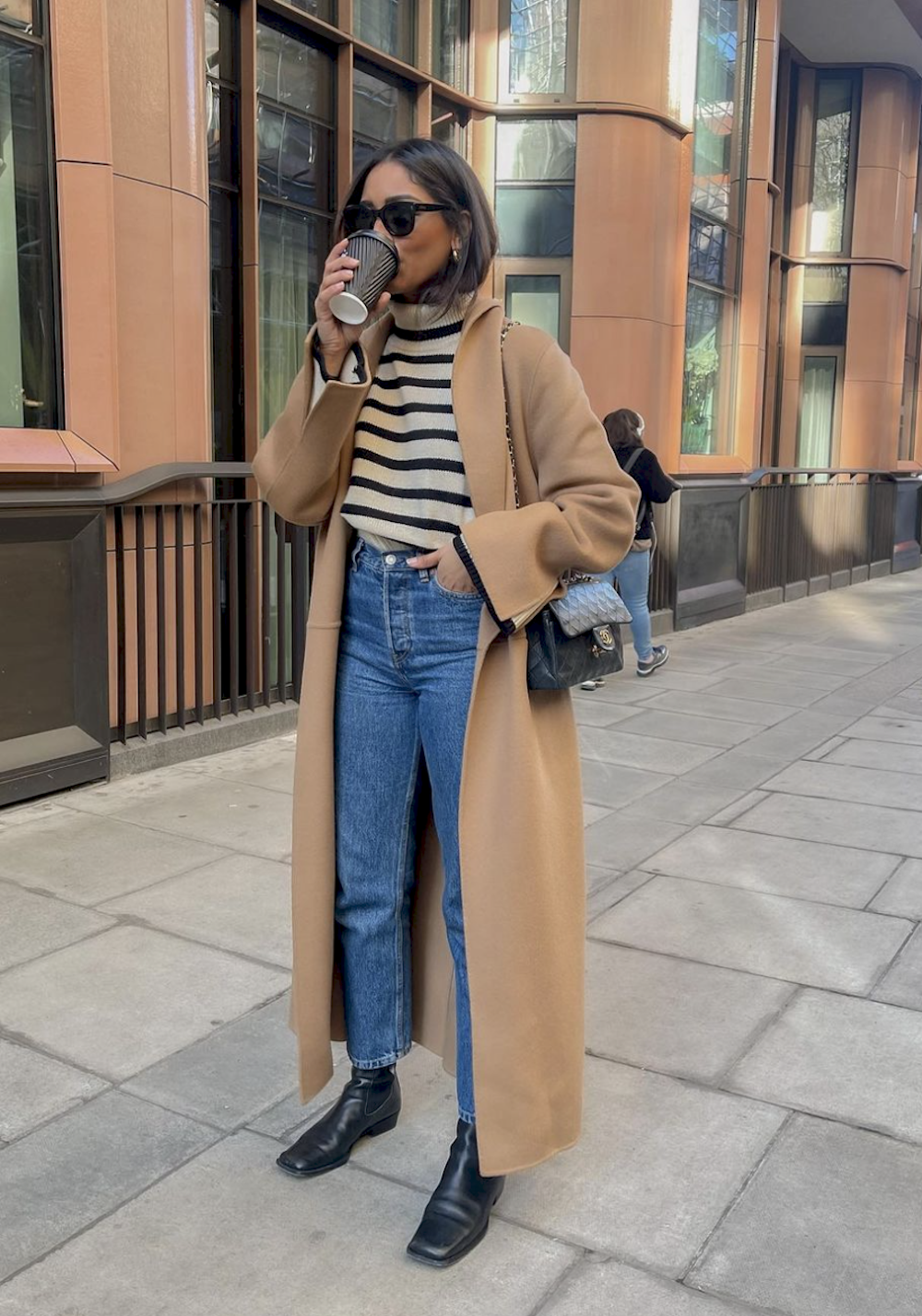 image of a woman in a long camel coat, striped sweater, blue jeans, and black boots