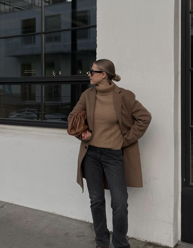 woman wearing a tan jacket over a camel turtleneck with black jeans