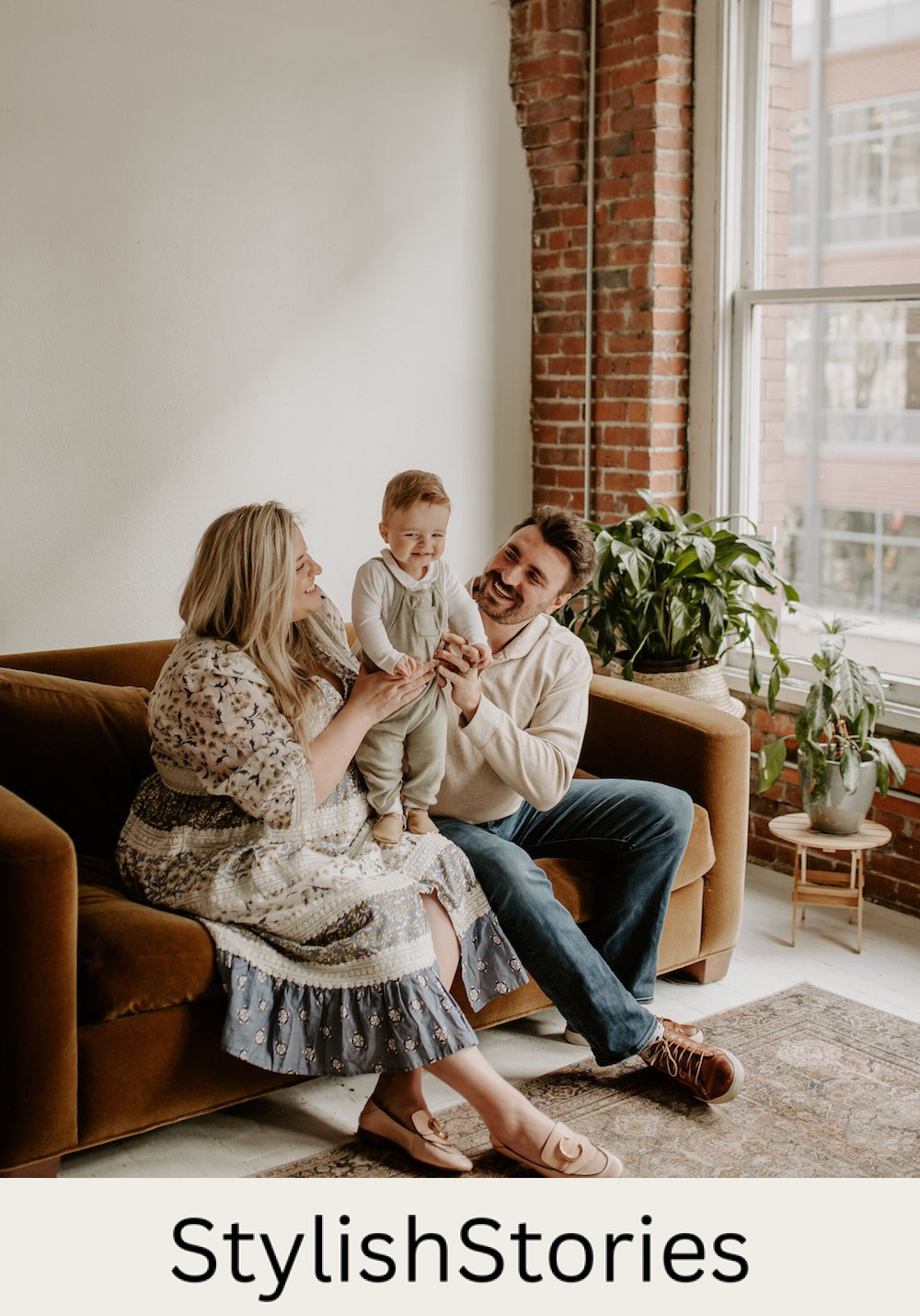 image of a family of three sitting on a velvet brown sofa in a loft wearing neutral tones and the mom in a floral blue and ivory dress