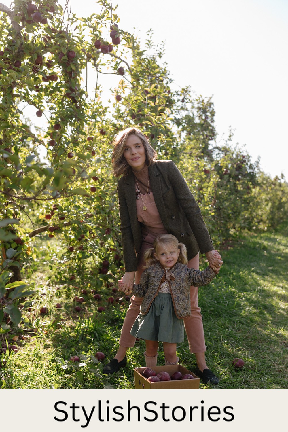 image of a mother and daughter in an apple orchard in the fall wearing neutral and dark pastel color outfits