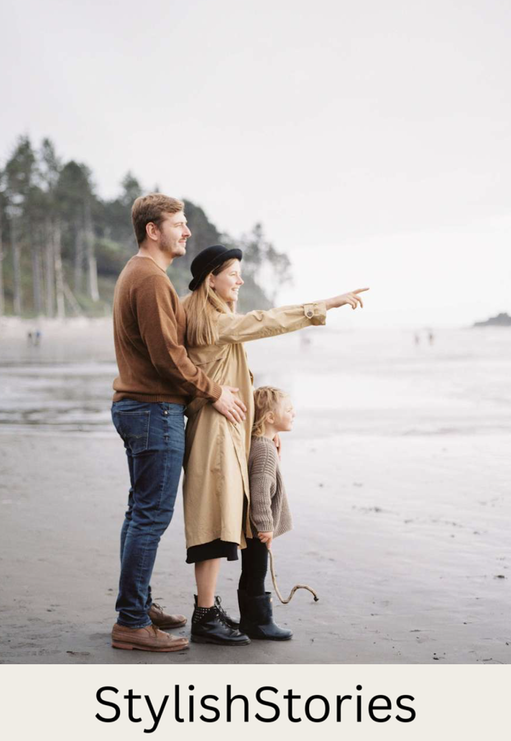 image of a family with a dad, mom, and small child wearing neutral clothing and boots standing on the beach looking out to the water in the fall