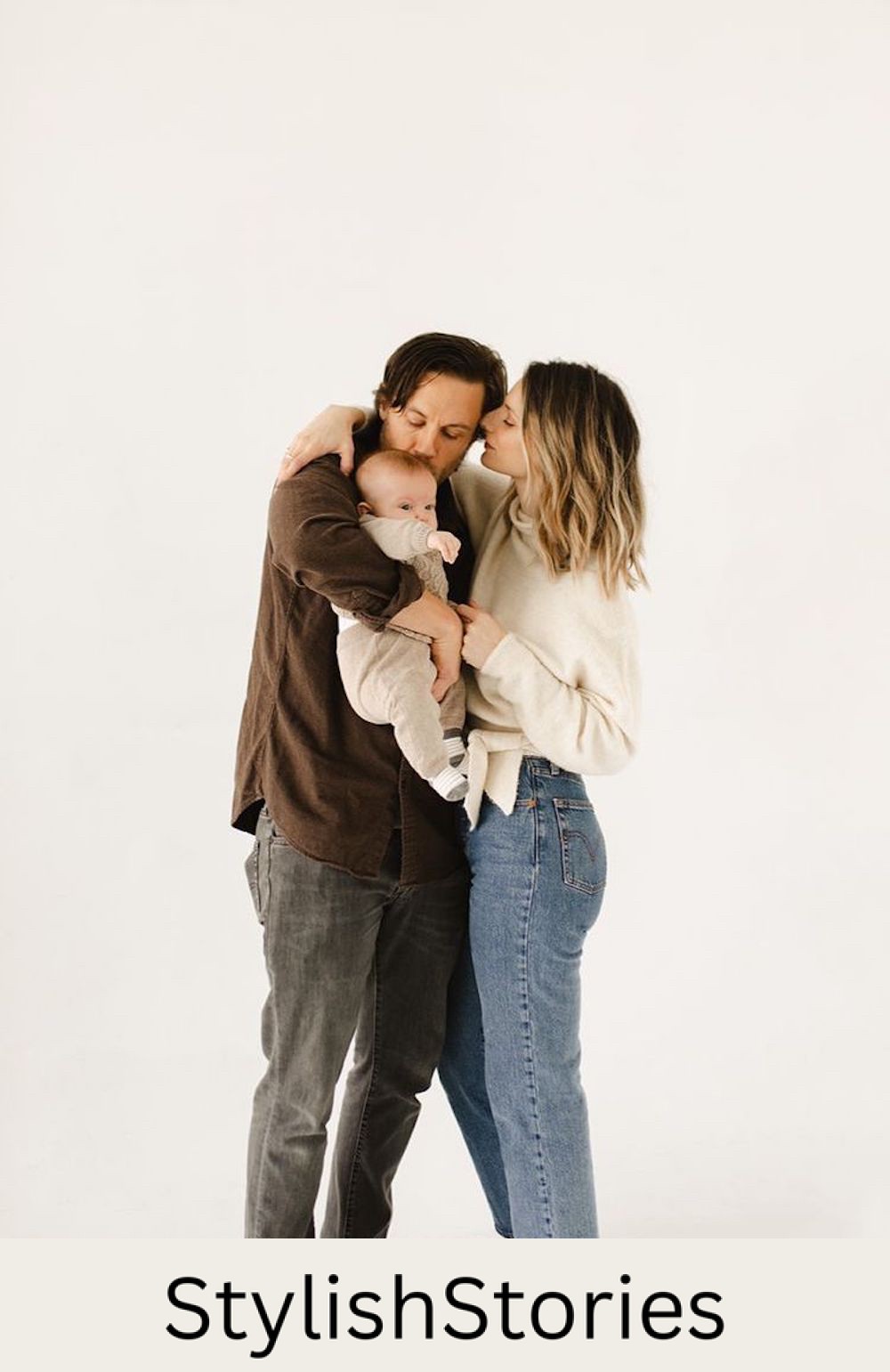 image of a family with a woman, man, and baby against a white wall for a family photoshoot, wearing jeans and casual tops