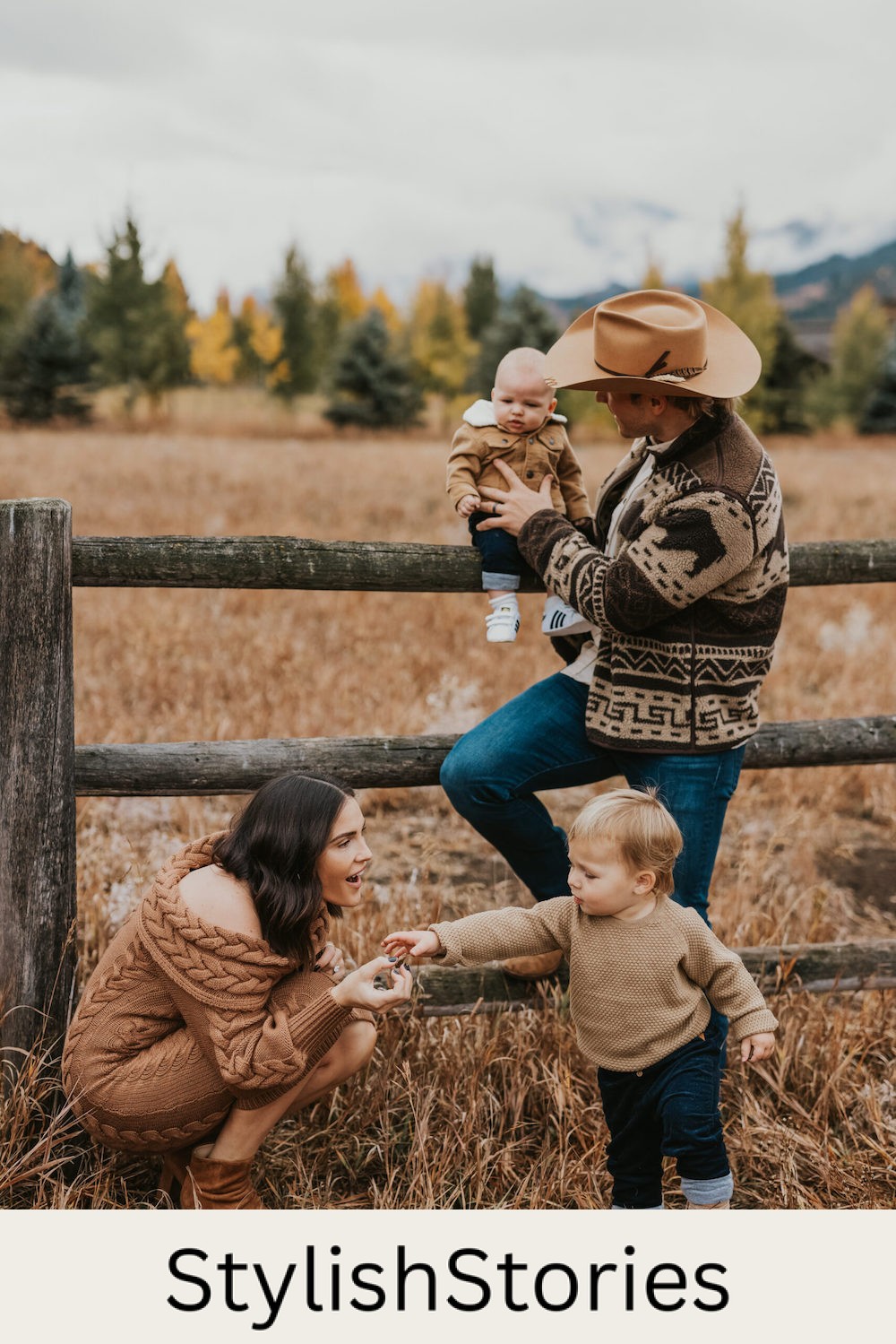 image of a family with a man, woman, toddler, and baby against a wooden fence in a field wearing neutral clothing and the man is in a cowboy hat