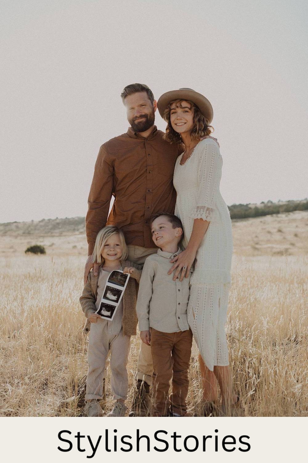 image of a family with a man, woman, and two young boys standing in a wheat field wearing ivory and brown earth tone clothing