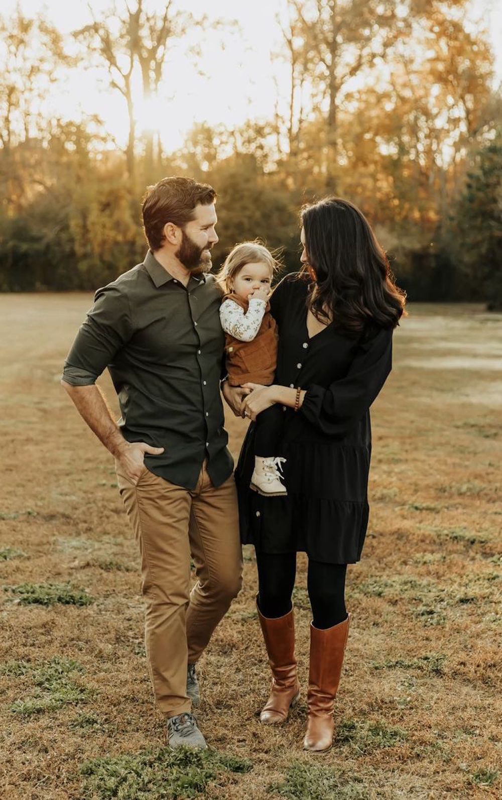image of a family with a man, woman, and baby taking fall family photos wearing black, camel, green, and rust colors
