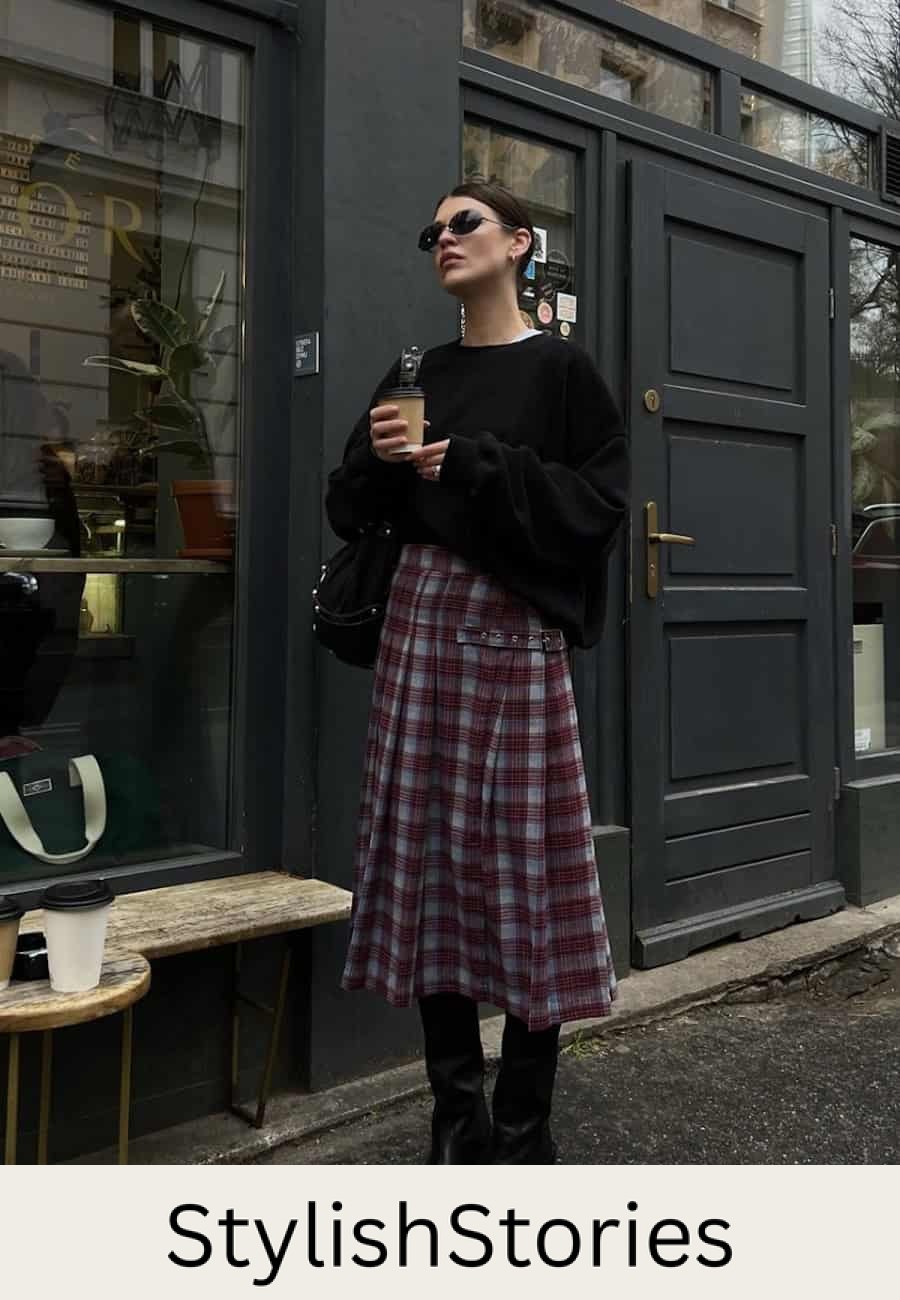 Woman wearing a plaid midi skirt with a black oversized sweater and black boots.