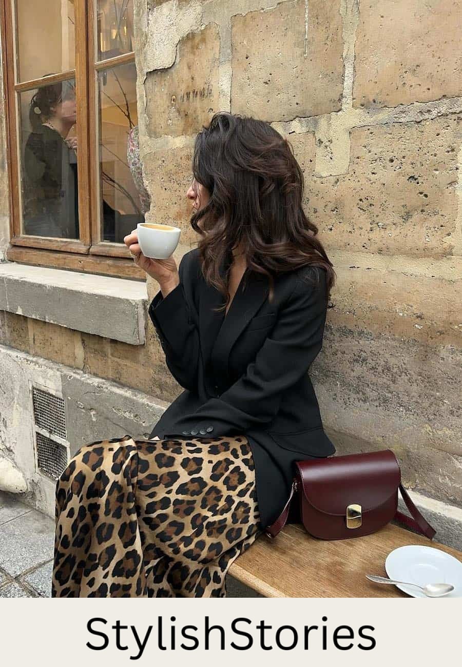 Woman wearing a leopard print midi skirt with sneakers and a black blazer.