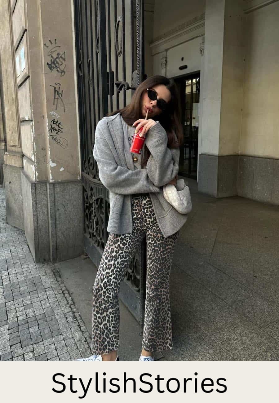 Woman wearing leopard print jeans with sneakers, a graphic tee and a cardigan.