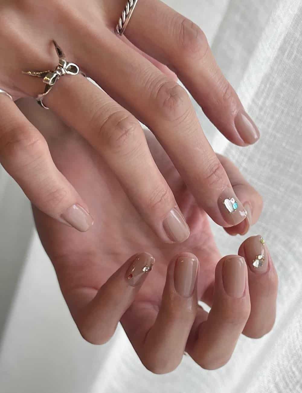 short squoval nails painted a nude polish with gem accents
