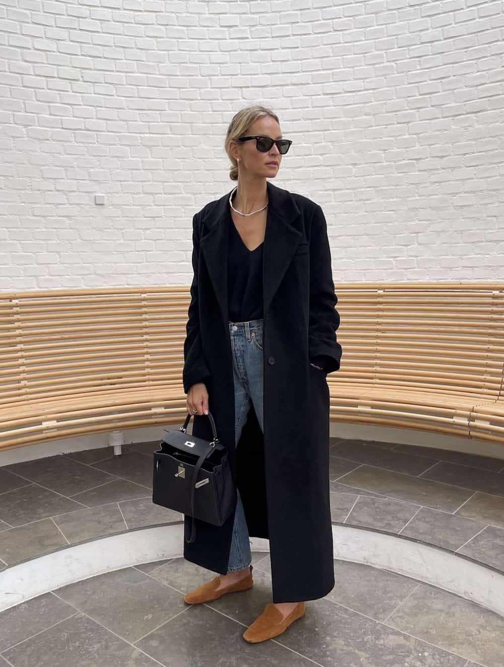 Woman wearing jeans, a black sweater and a black coat.
