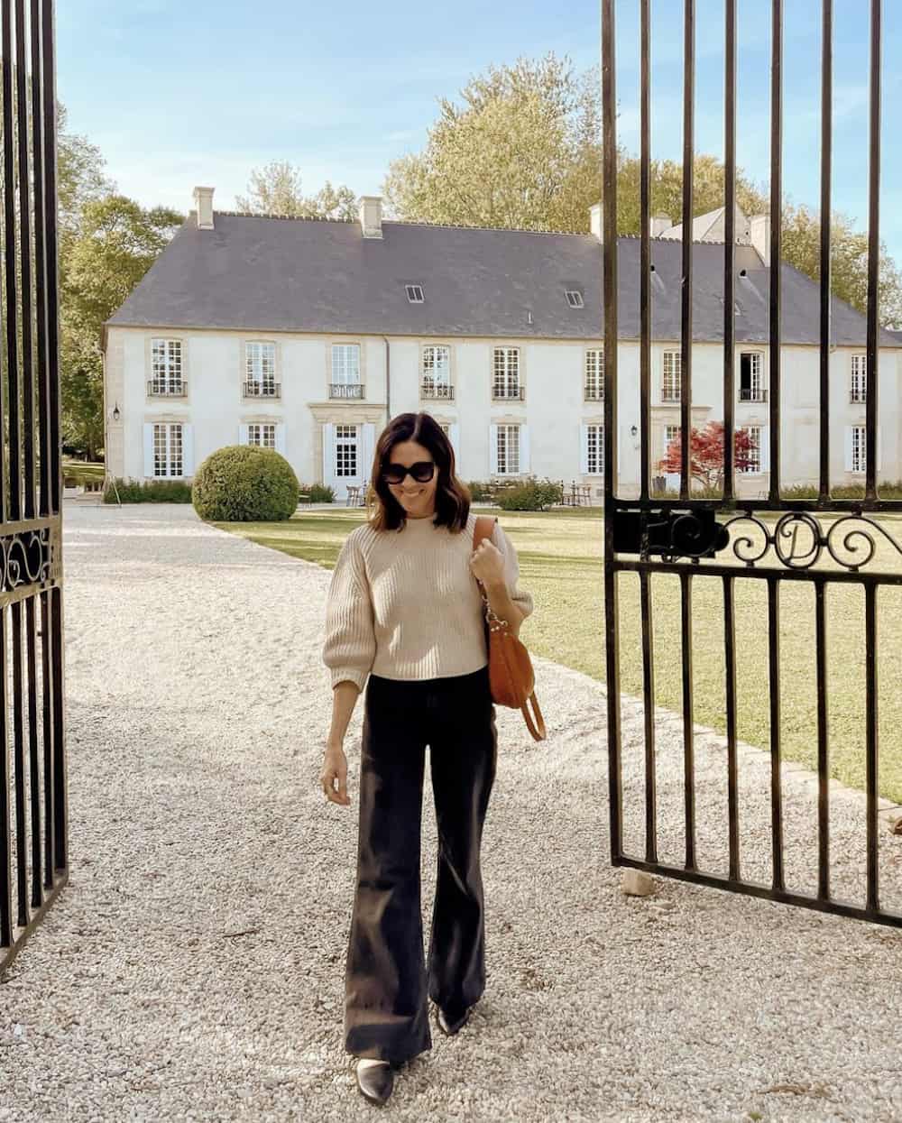 Woman wearing black, wide leg pants and a cream sweater.